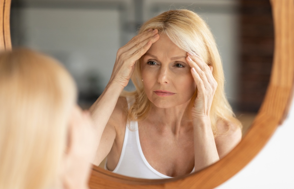 Vrouw kijkt vermoeid in de spiegel en raakt haar voorhoofd aan
